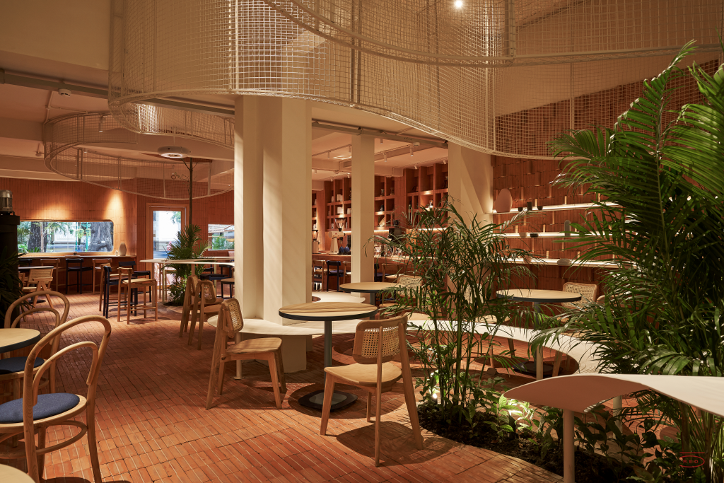 Sảnh ăn ngập nắng giờ vàng của Anh Coffee Roastery — mái lưới kim loại uốn lượn, ghế mây, bàn đá cẩm thạch và cây xanh