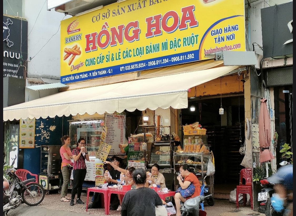 Bánh Mì Hồng Hoa storefront by day — diners at red plastic tables out front