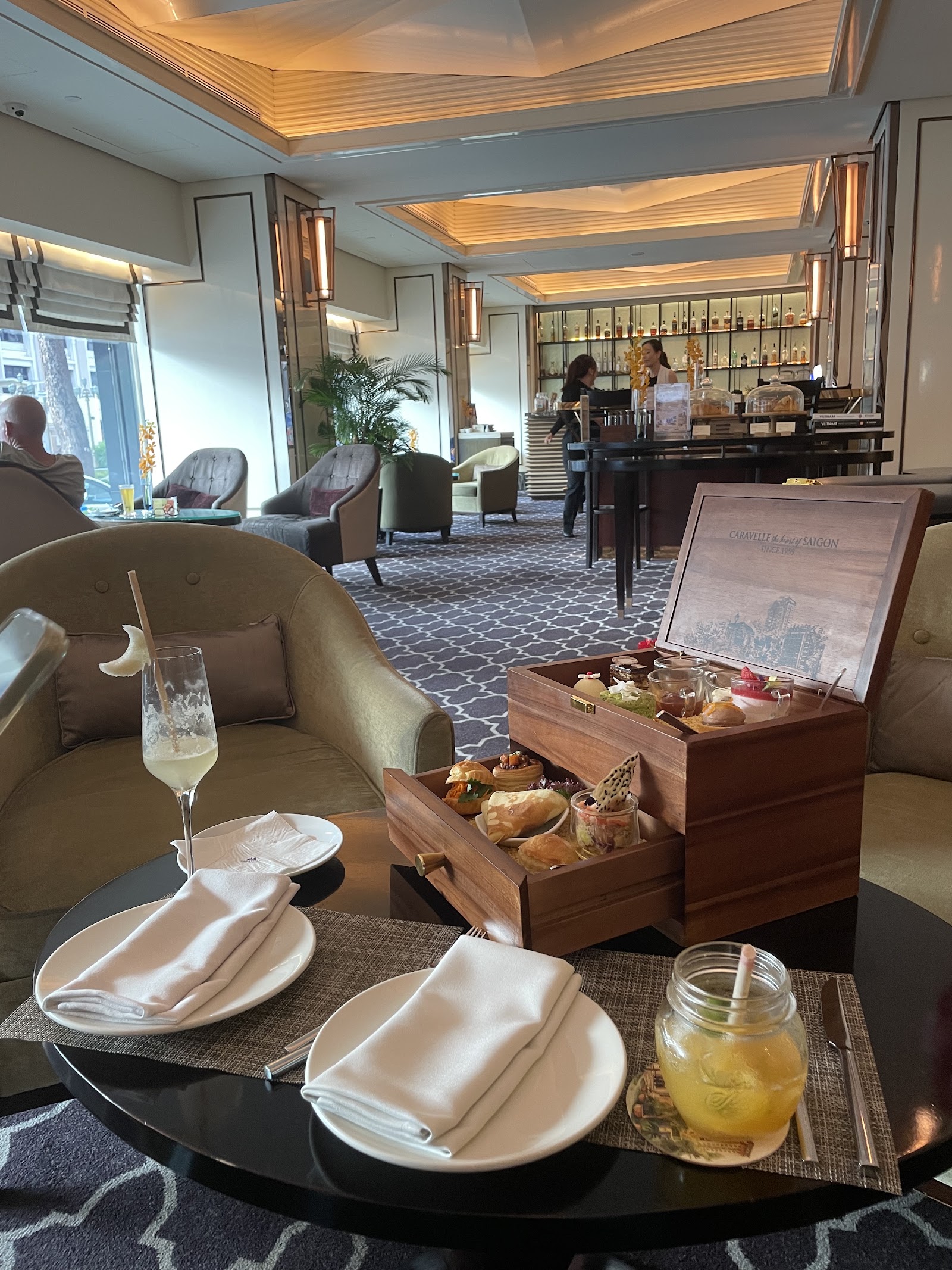 'Caravelle — the heart of Saigon'이 새겨진 나무 박스의 애프터눈 티: 세이버리, 페이스트리, 디저트 컵, 뒤편의 바
