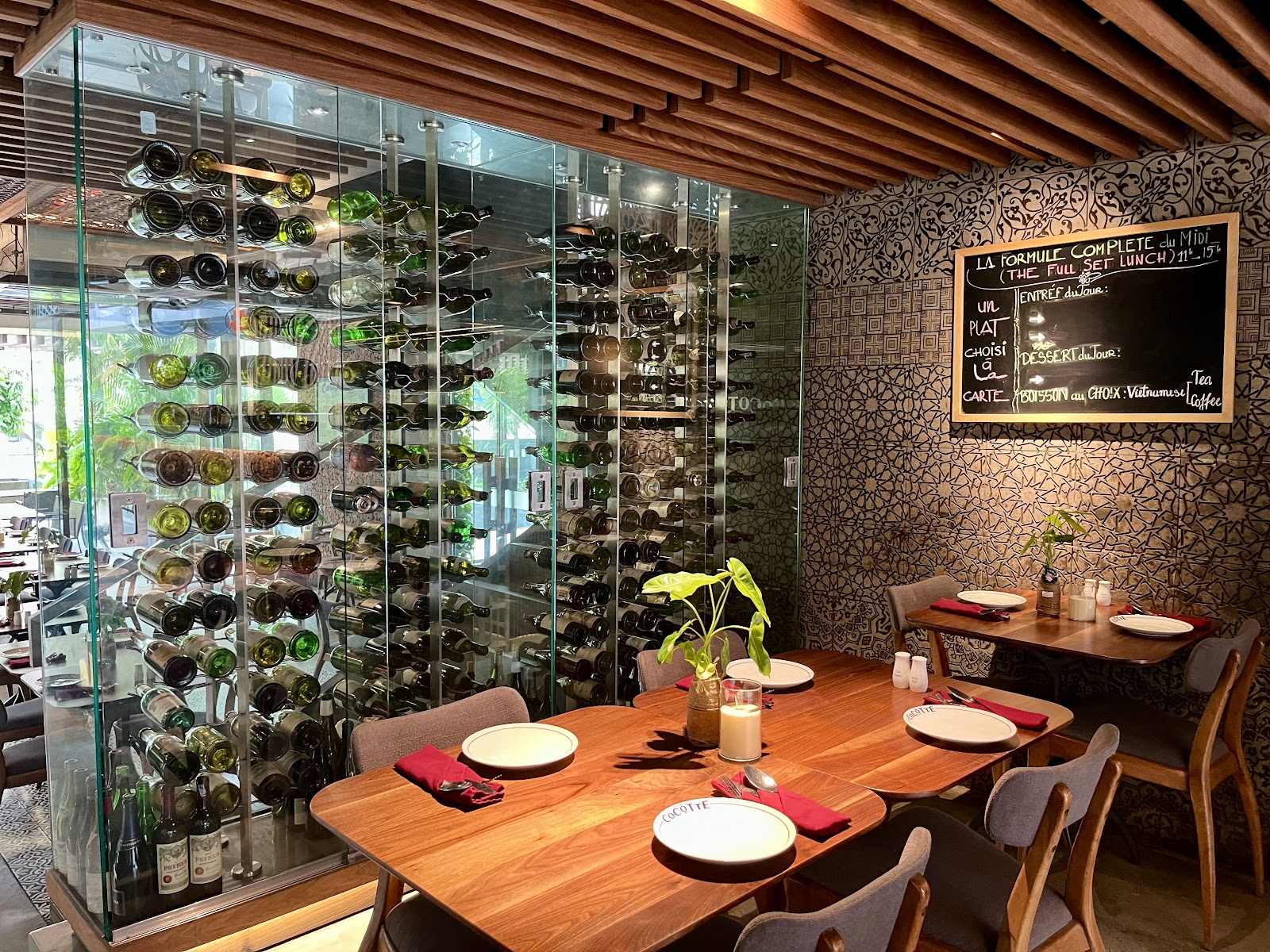 The floor-to-ceiling glass wine-cabinet wall with bottles stacked inside; wooden tables with red napkins in front