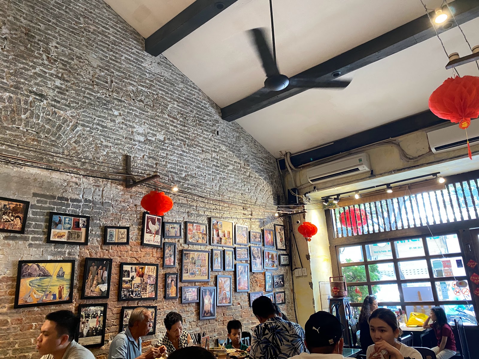 Không gian quán: tường gạch thô phủ ảnh cũ đóng khung, đèn lồng đỏ