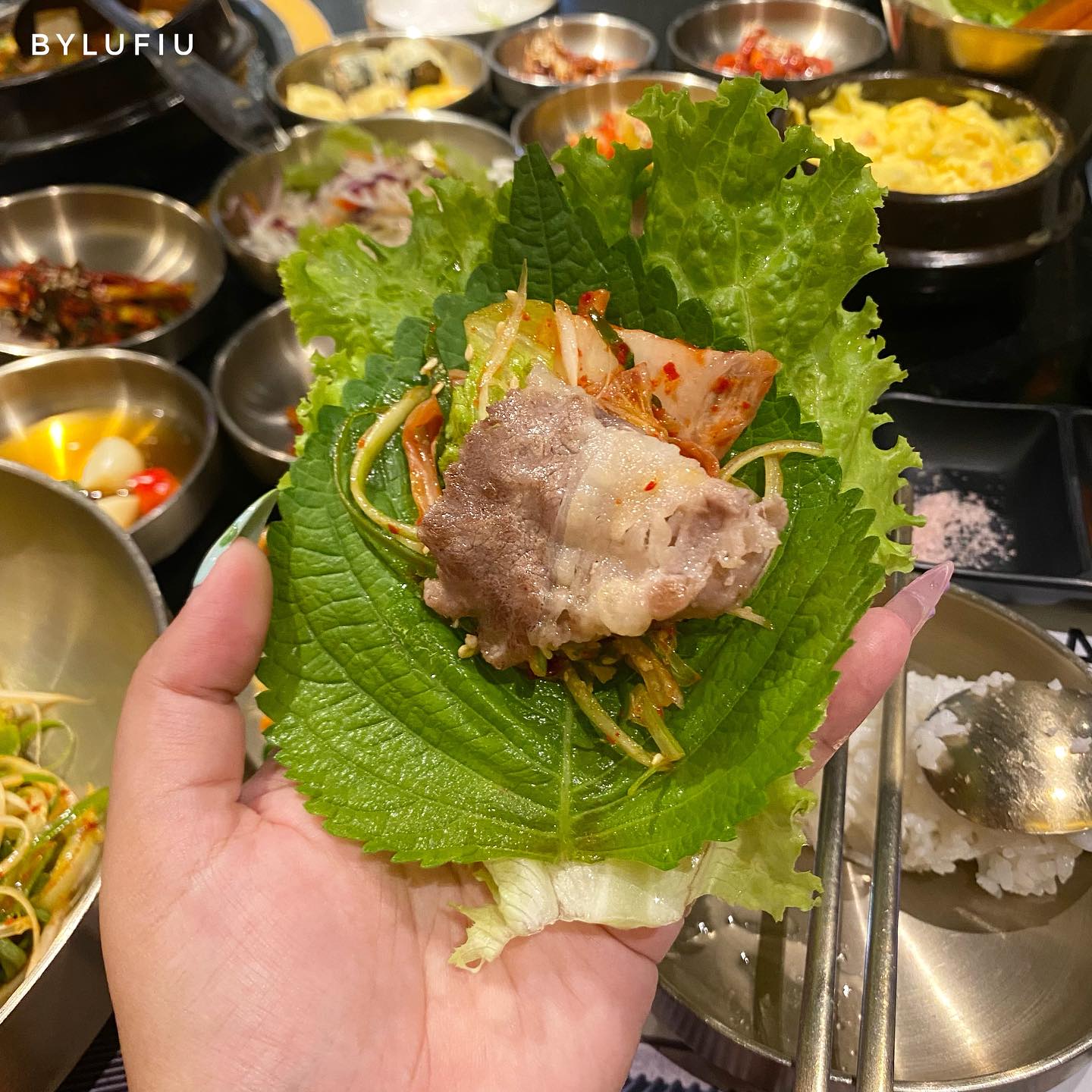 A hand-held ssam wrap — grilled meat, kimchi and banchan