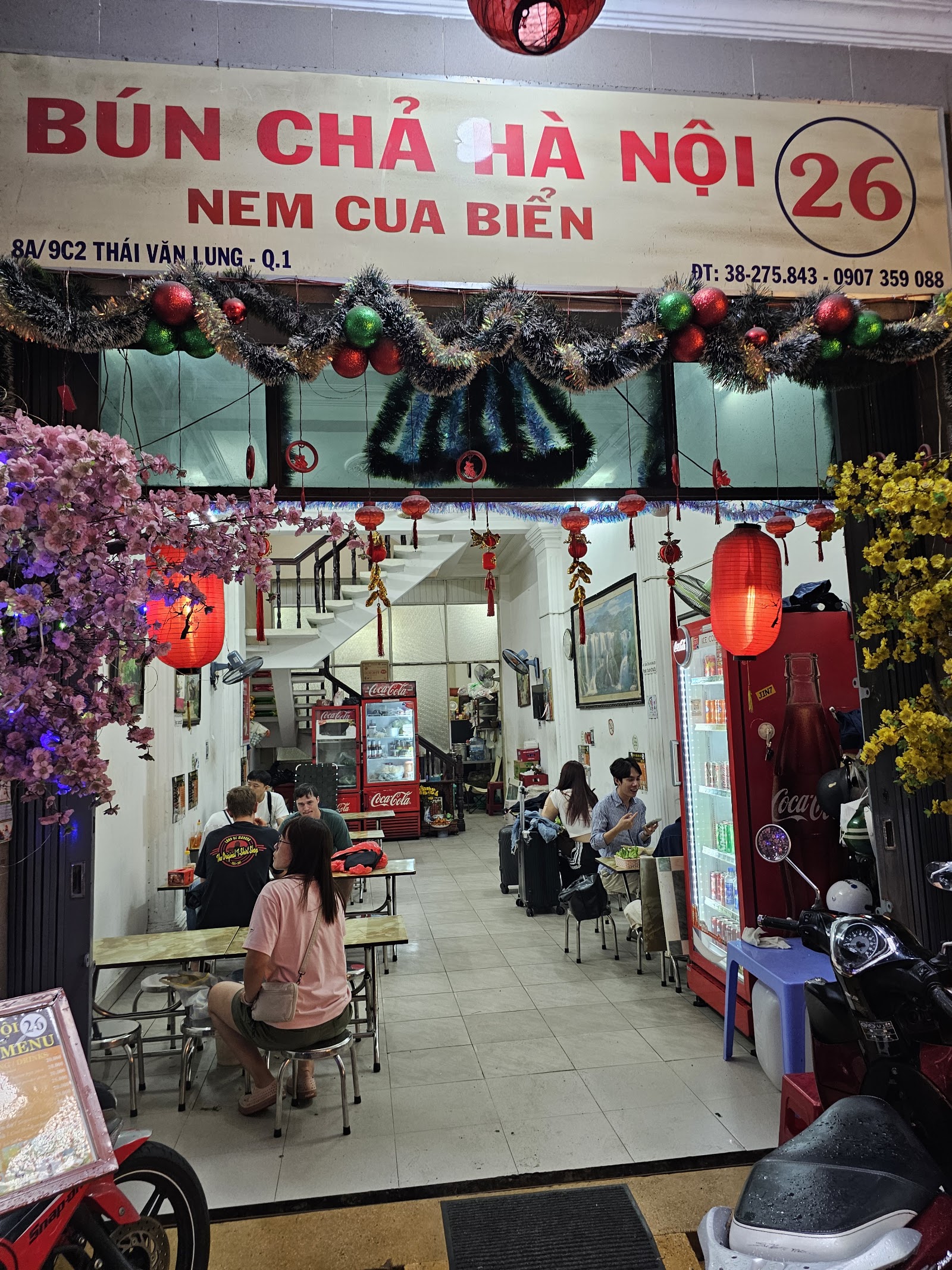 저녁 매장 외관 — 빨간 BÚN CHẢ HÀ NỘI 26 간판, 빨간 등불과 복숭아나무