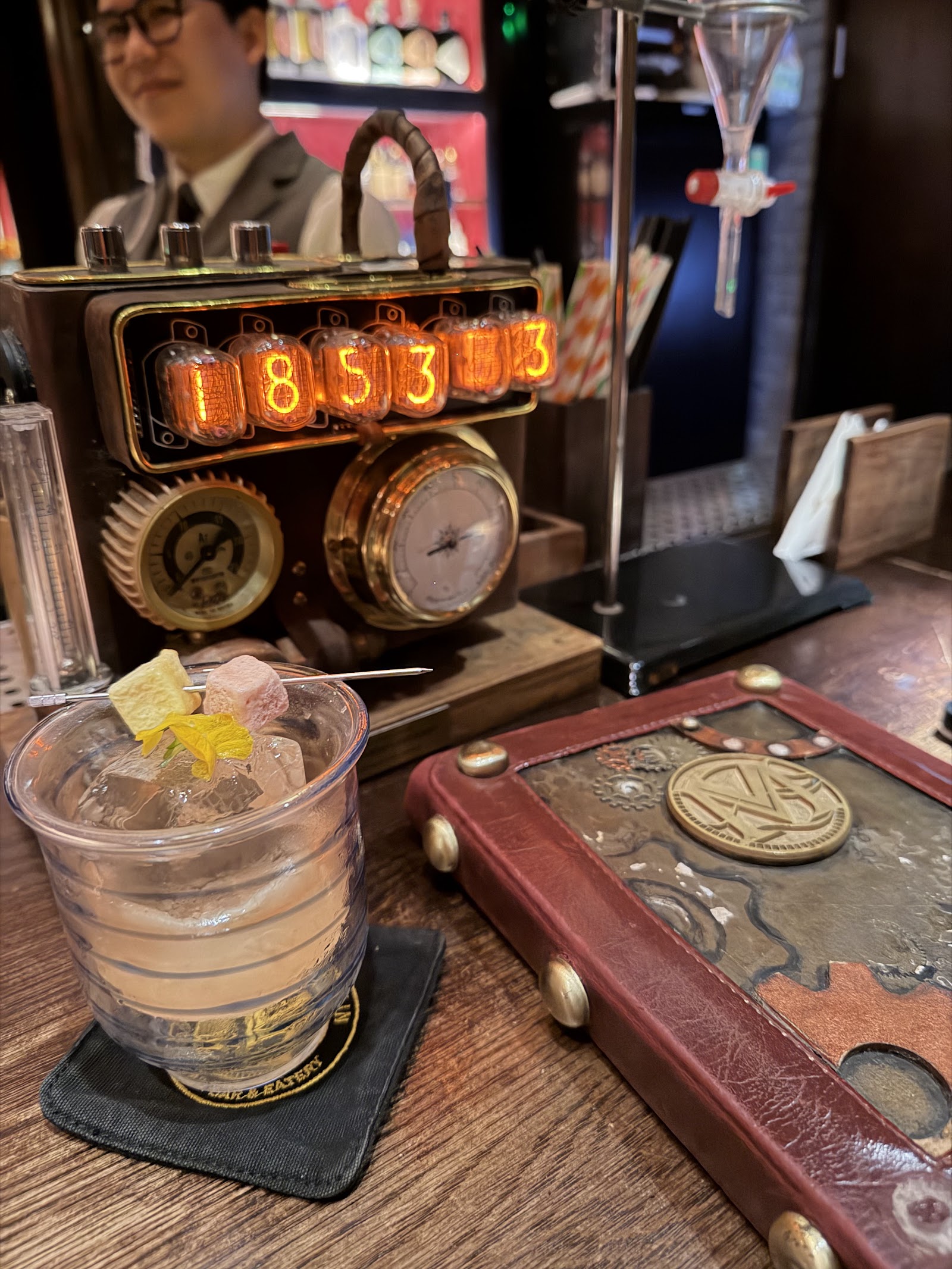 The alchemy bench — nixie-tube clock, pressure gauges, a signature serve