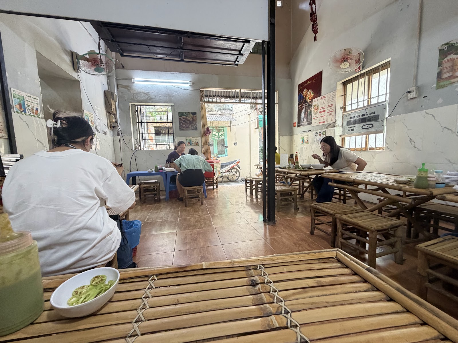 Inside the shop: bamboo tables and stools, guests mid-meal, menu posters on the wall