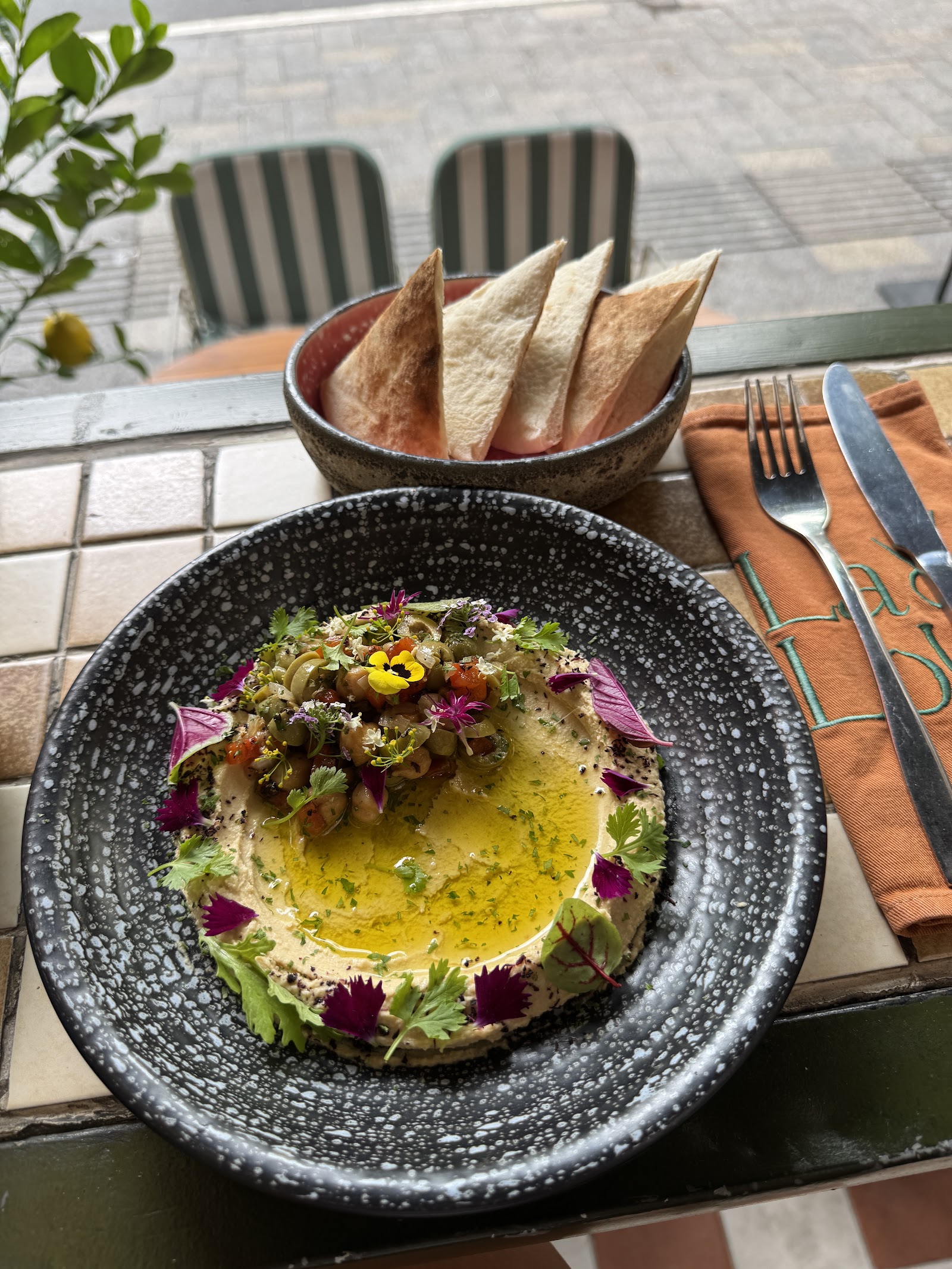 Hummus rưới dầu ô liu với rau thơm, hoa ăn được và bánh pita