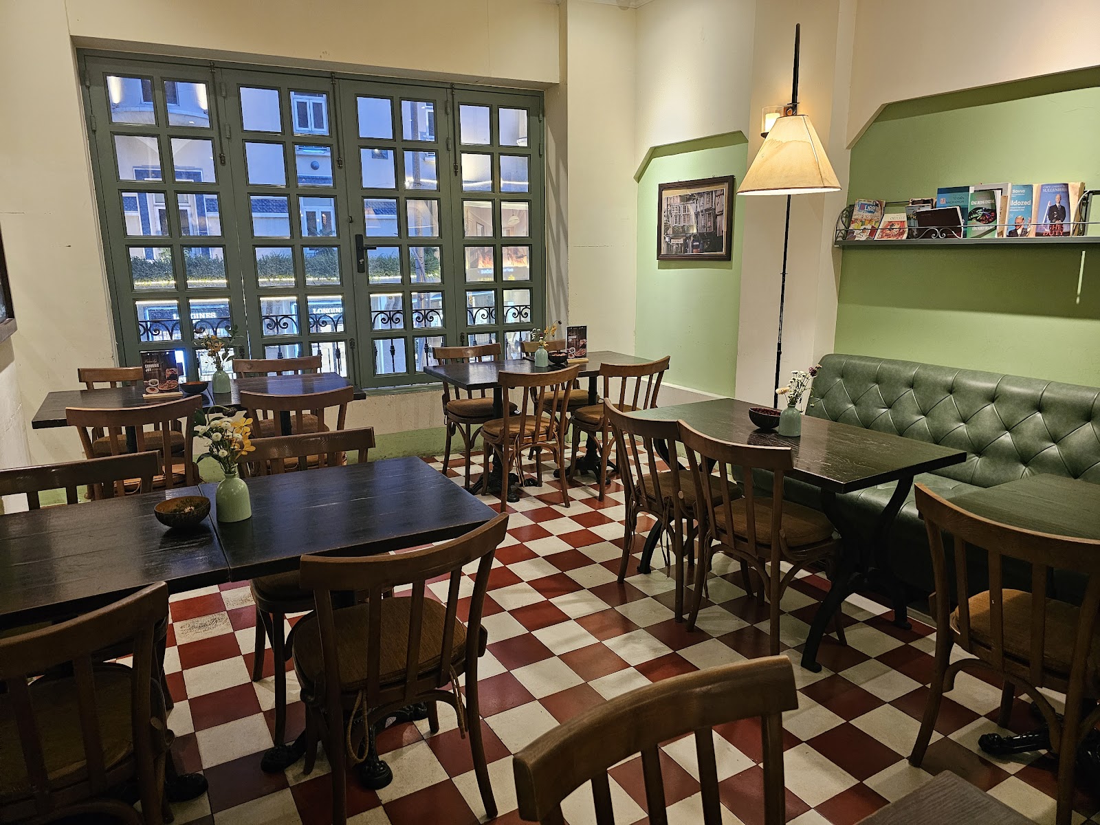 The booth room — the green tufted-leather booth, dark wood tables and chairs, the terracotta checkerboard floor, French doors to the street