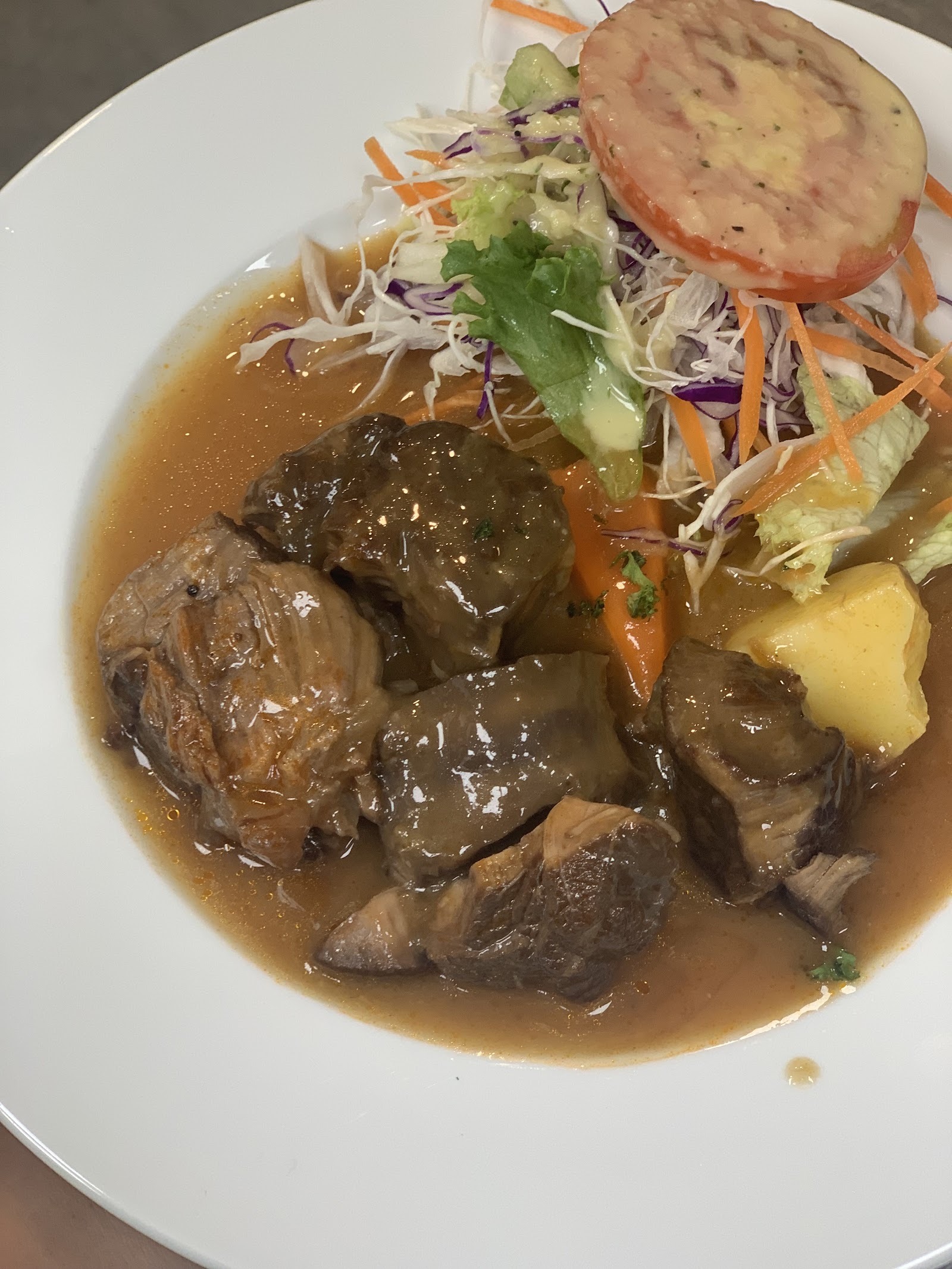 Beef stew chunks in brown sauce with salad, tomato and potato