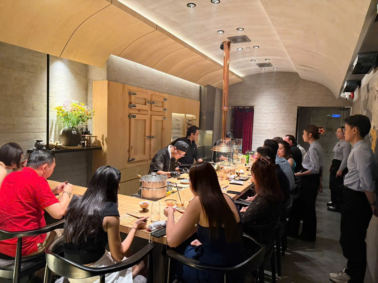 The Omakase K counter at night — diners along the pale-wood counter, chefs at work