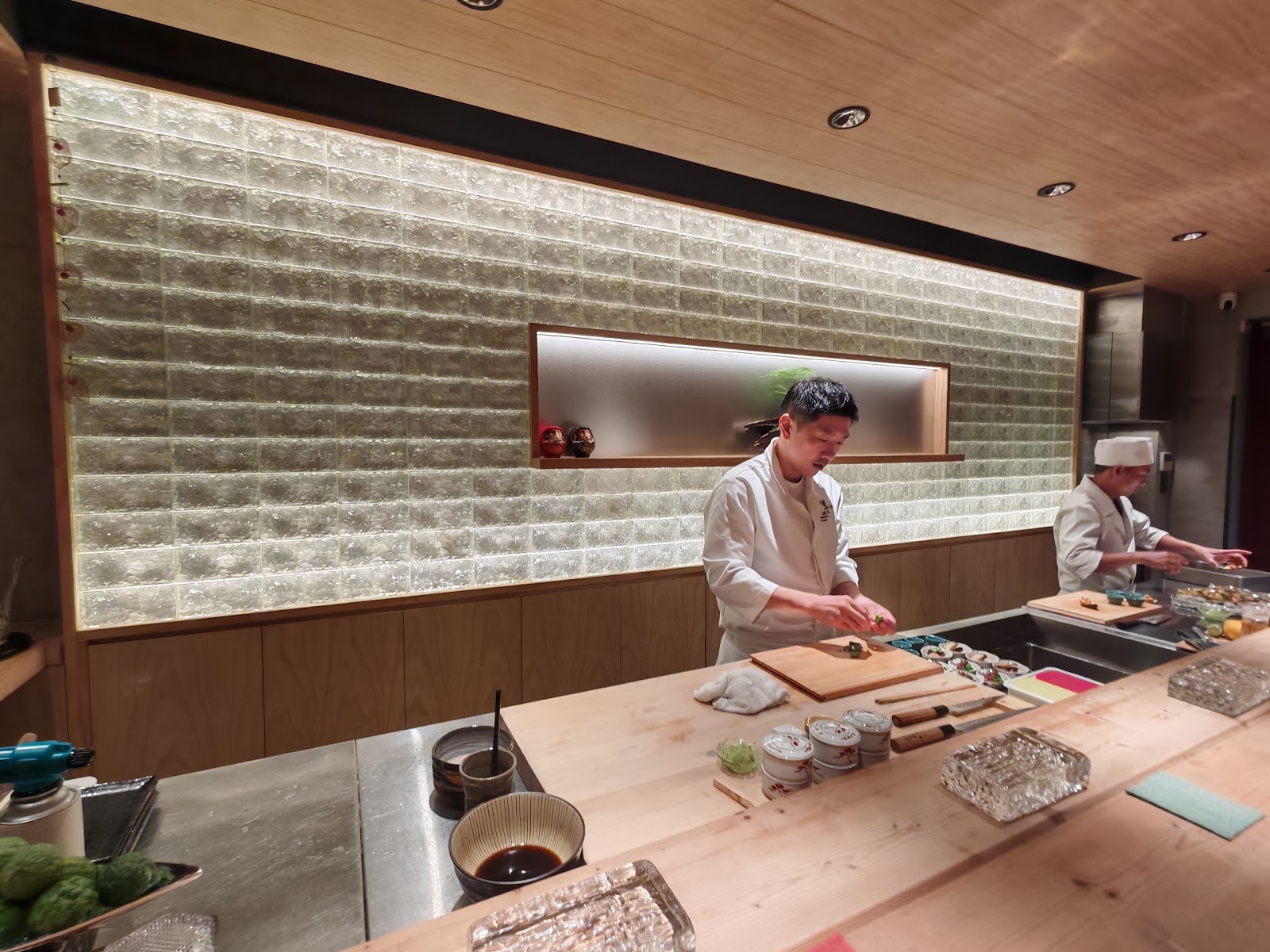The chef at work behind the counter — glowing glass-block wall, hinoki wood