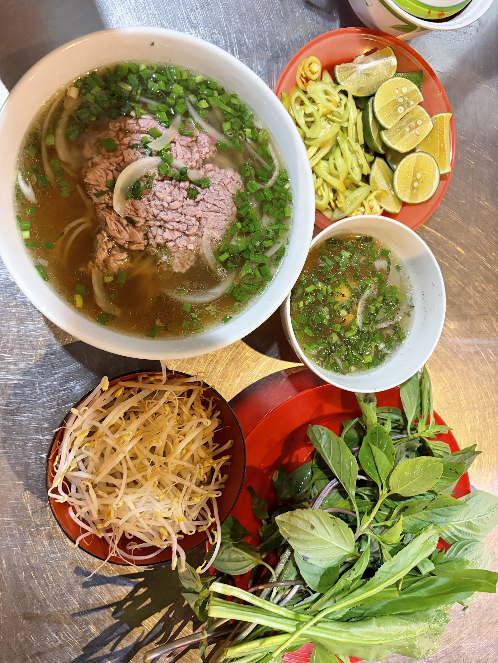 The evening shift table: full rare-beef bowl, sprouts, lime and chili, herb plate — on steel