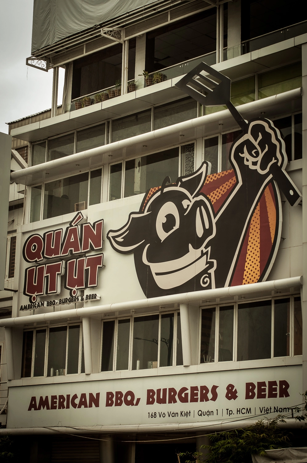 Quan Ut Ut logo: a pig holding a grill spatula, reading American BBQ & Beer