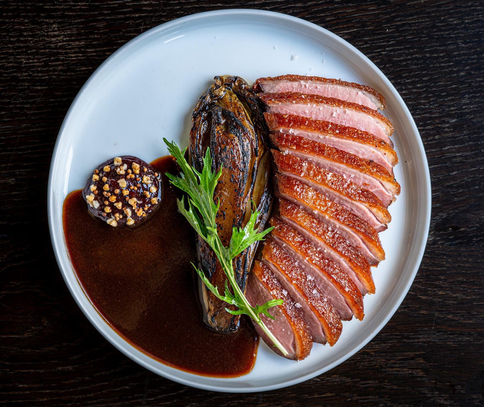Aged duck breast with charred endive on a dark plate