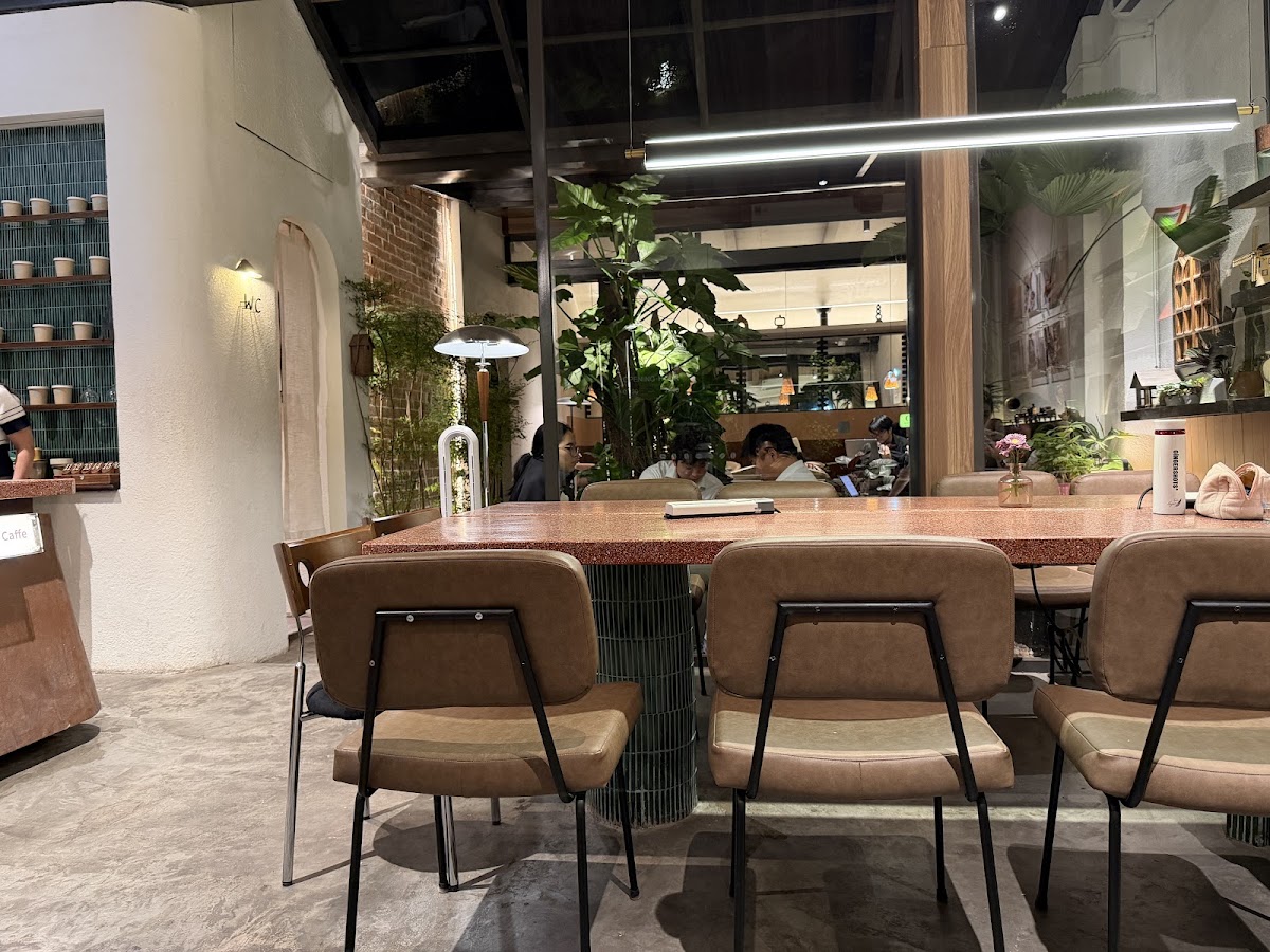 Sancara Caffe — sảnh giếng trời: ghế da nâu, bàn terrazzo, cây xanh