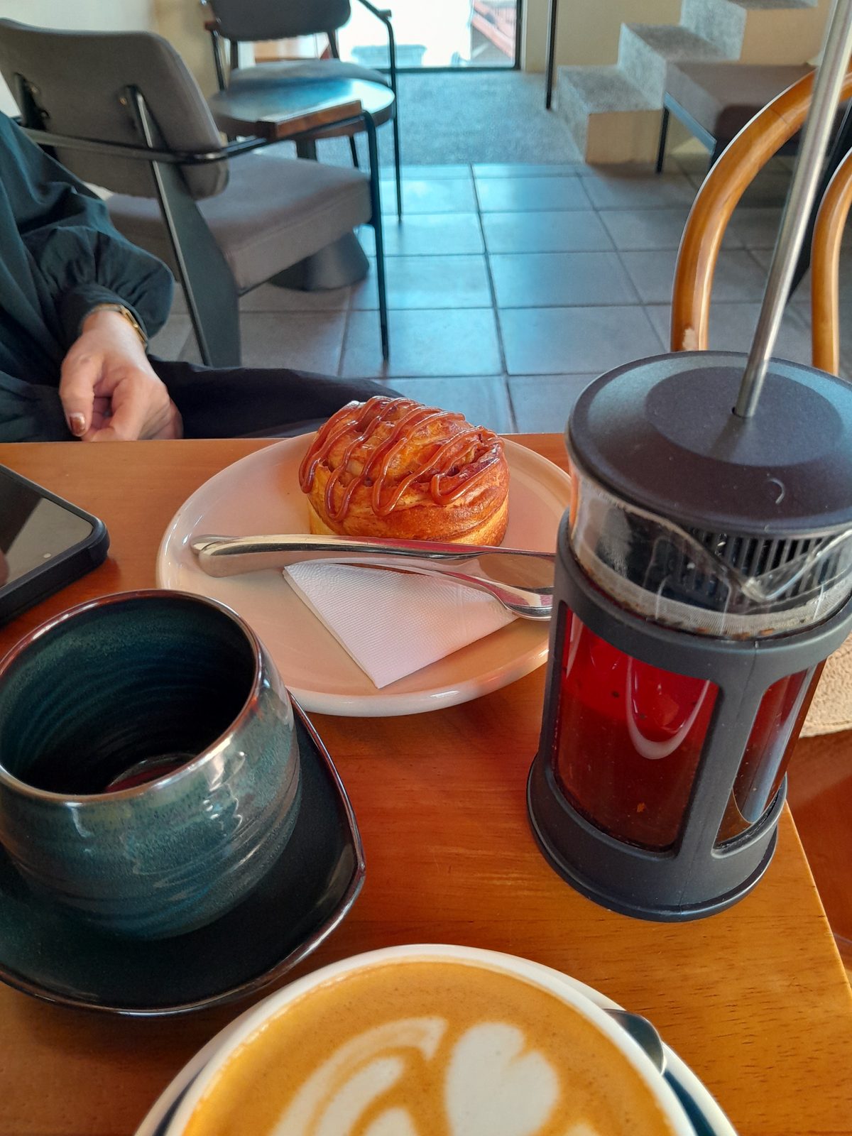 A real table at Saveur Café: latte art, dark teal ceramic cup, caramel-glazed pastry, tea french press (Frederic Fayard, Feb 2026)