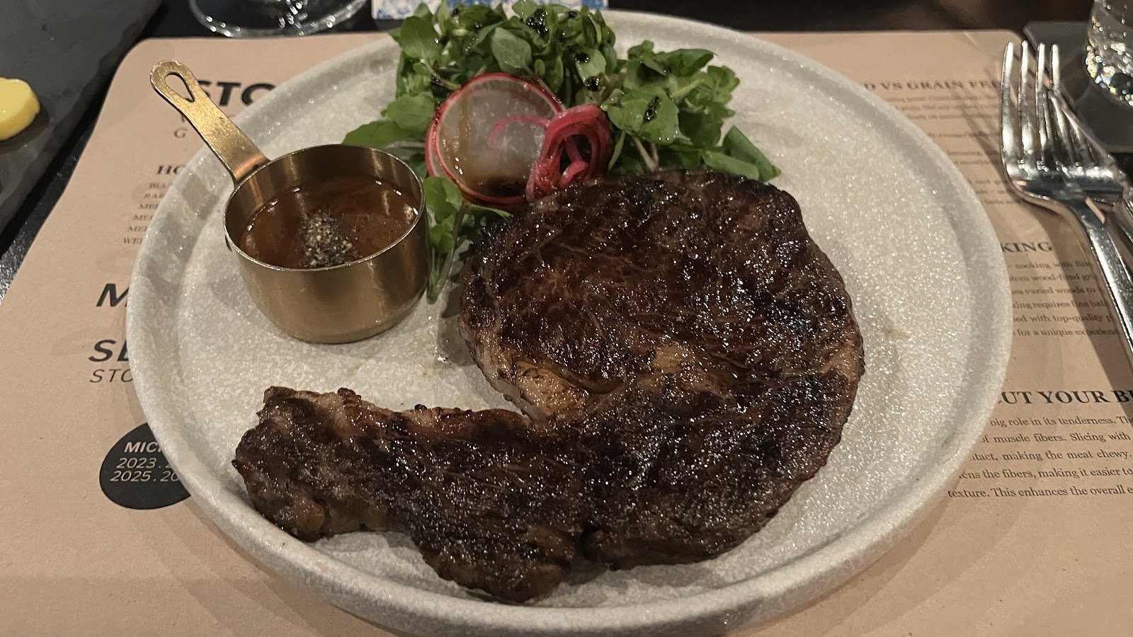 The grilled steak on stoneware with its brass sauce pot and greens