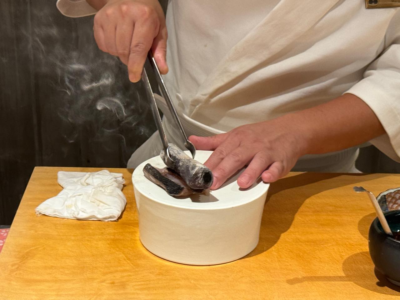 The chef's hands finishing fish over binchotan smoke