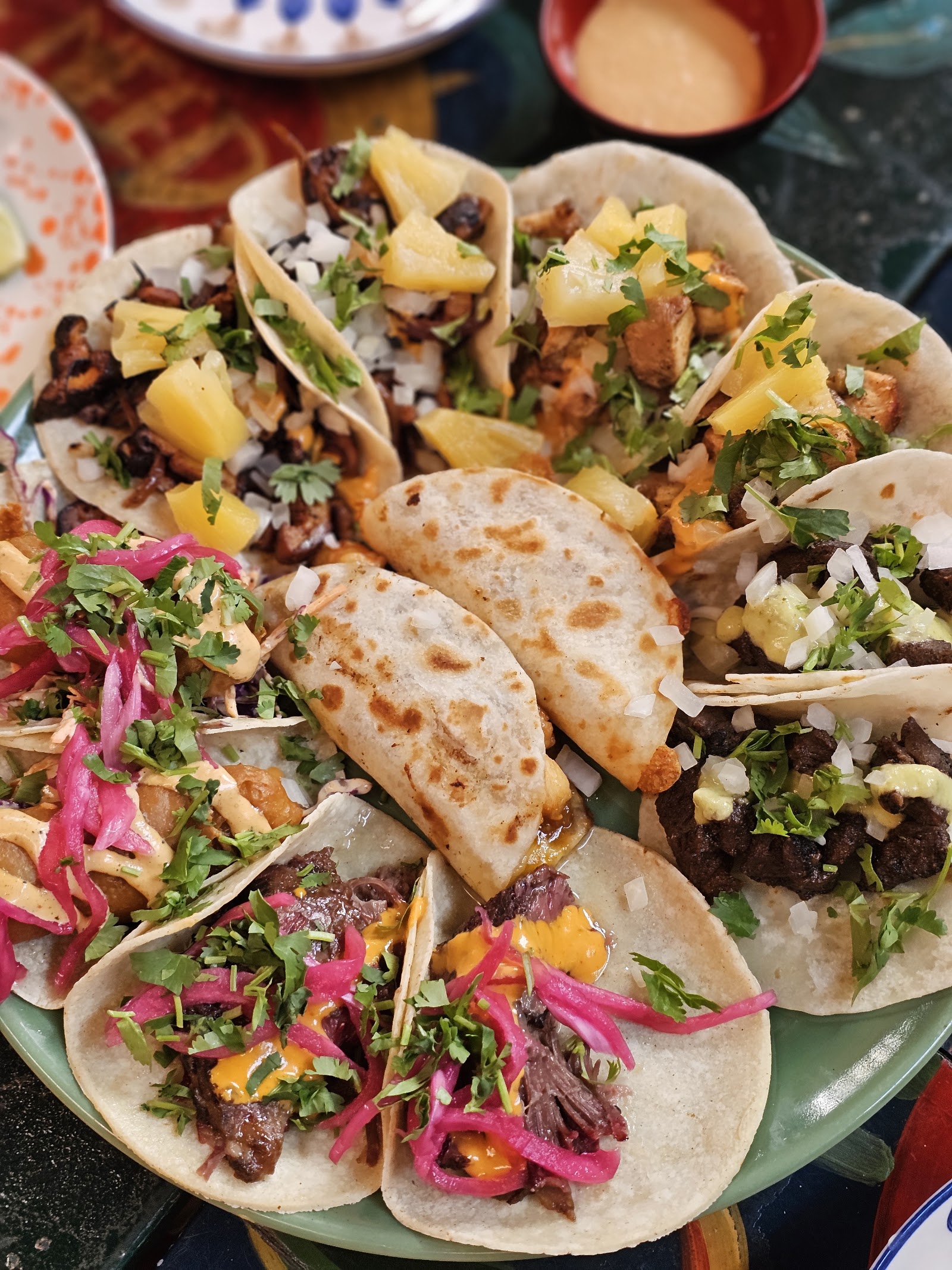 Đĩa tacos đường phố trong ảnh của quán — tortilla gấp, dứa, hành tím muối chua