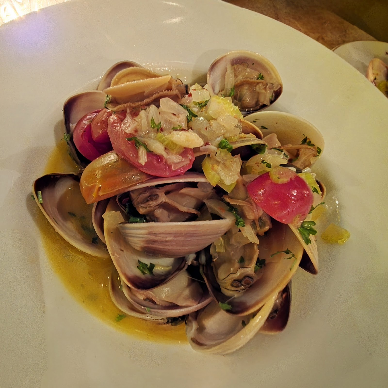 Sautéed clams with red cherry tomatoes and herbs in a white bowl