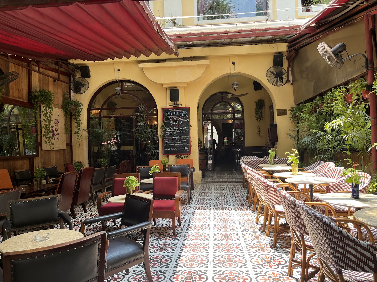 The covered courtyard with two grand arches, rattan and leather chairs, red patterned tiles, a chalkboard with happy-hour times