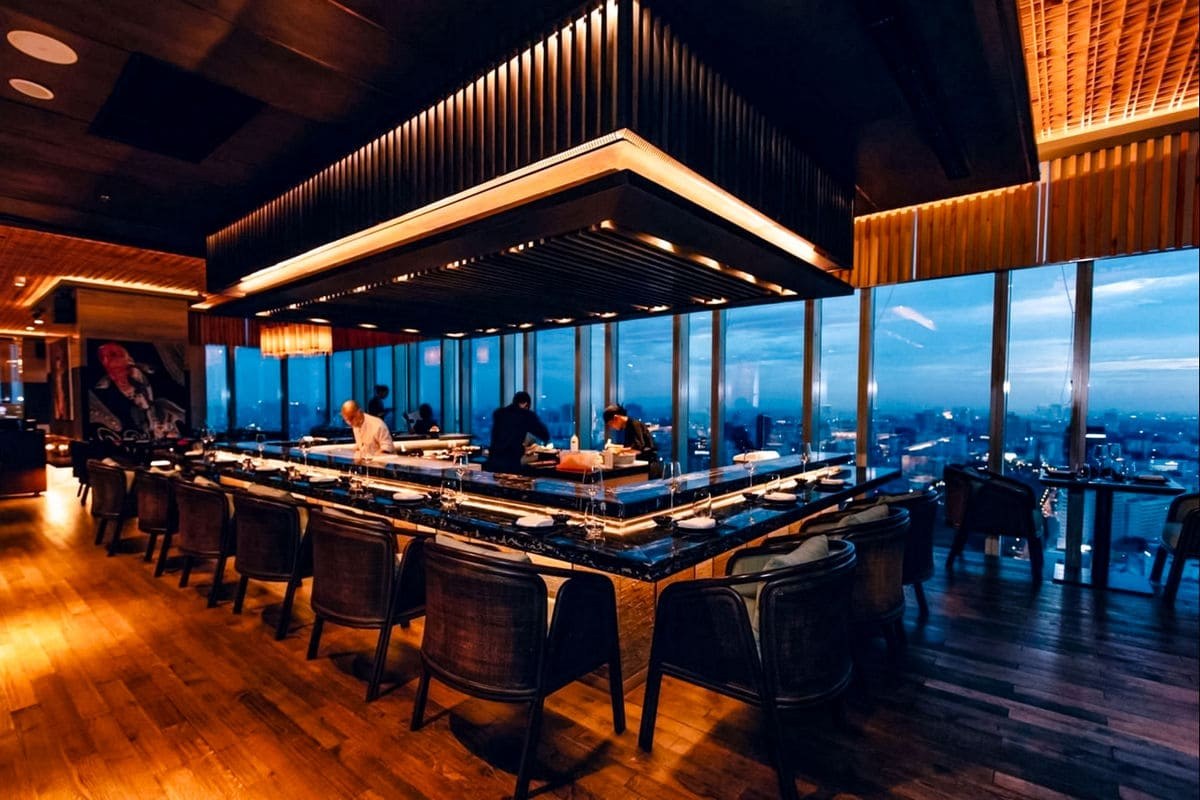Lounge Towa về đêm — các đầu bếp sau quầy, thành phố xanh thẳm sau lớp kính